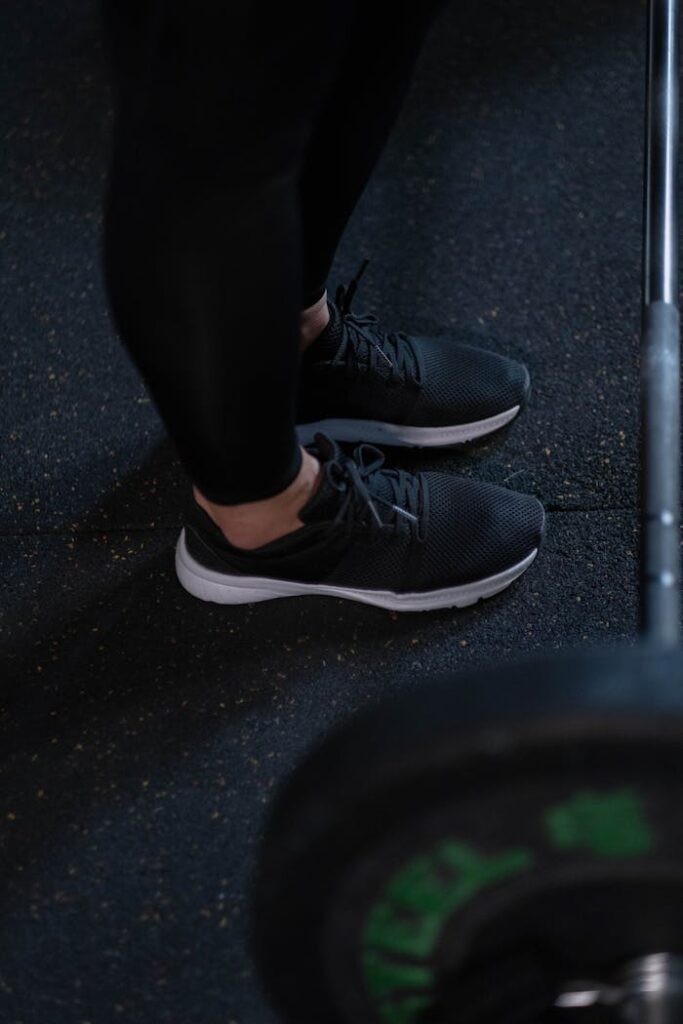 pexels-photo-7674491 Close-up of black sneakers and barbell on gym floor, perfect for fitness themes.